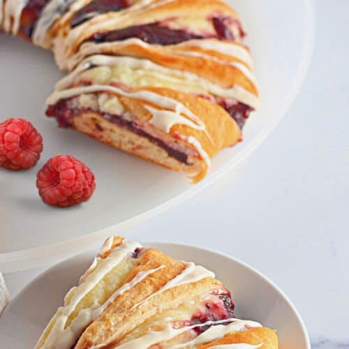 A slice of raspberry cake on a plate with a bowl of raspberries.