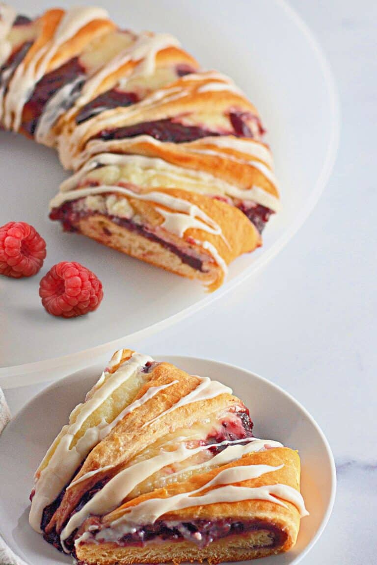 A slice of raspberry cake on a plate with a bowl of raspberries.