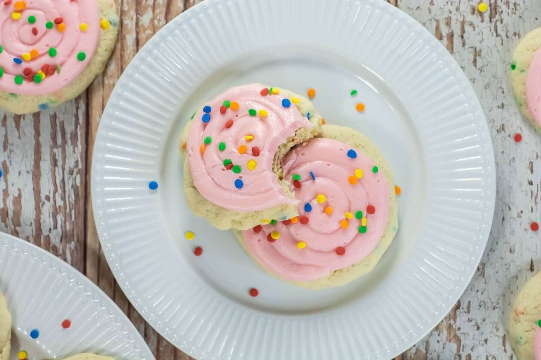 Crumbl-Style Confetti Cake Cookies topped with pink swirled frosting and sprinkles on a white plate.