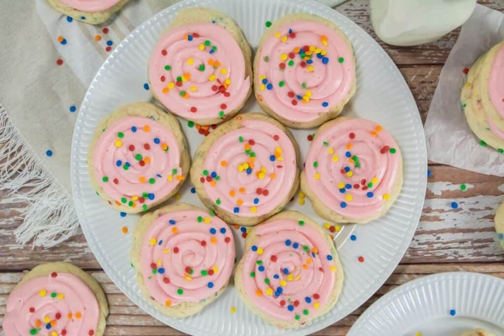 Pink frosted sugar cookies on a white plate with sprinkles.