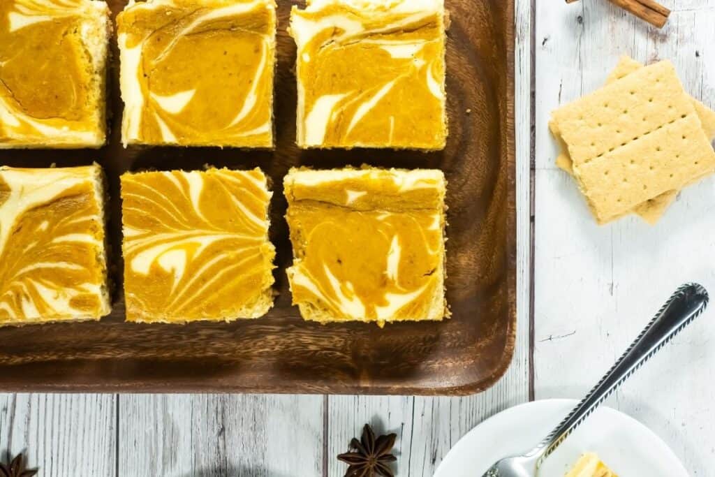 Six pieces of Pumpkin Cheesecake Bars on a wooden plate.