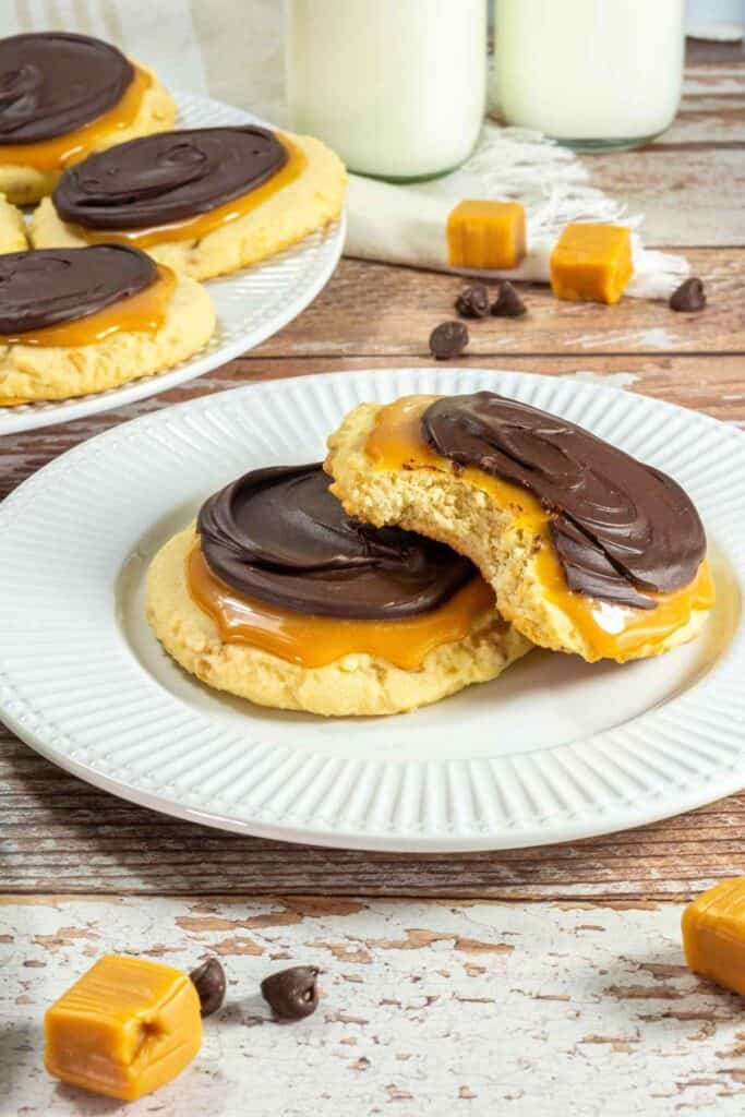 A white plate with two pieces of Crumbl Copycat Twix Cookies beside the other plate with cookies.