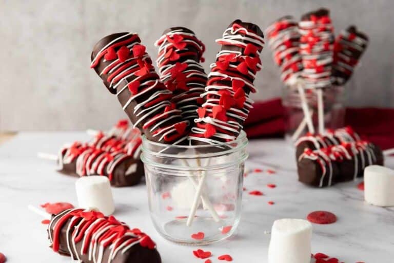 Delicious chocolate-covered marshmallow pops decorated with red and white icing and heart sprinkles, perfect for Valentine's Day.