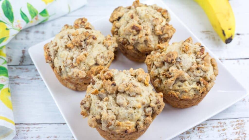 Four pieces of Banana Nut Muffins with Nutty Crumble Topping on a white plate.